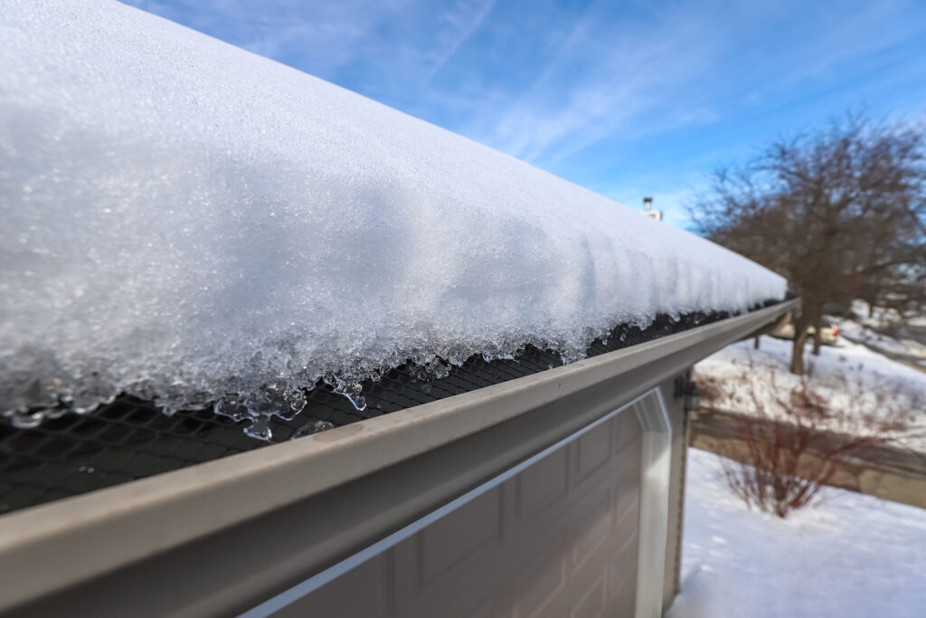 Heavy snow on roof and covering gutter in winter, causing potential damage that need Farmington roofing services.